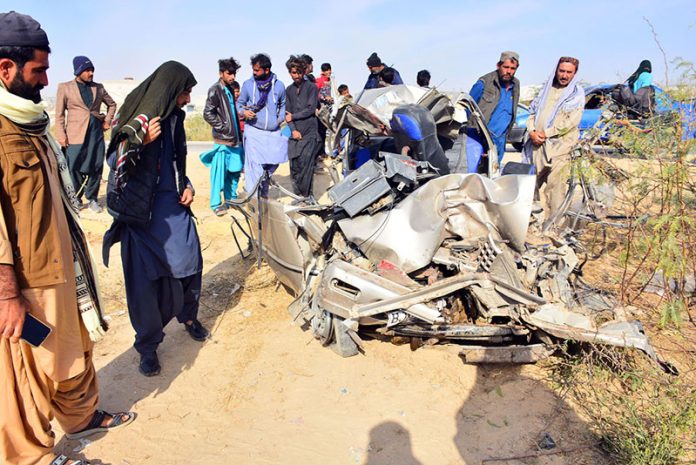 People gather around a damaged car after a truck-car collision on Kotri-Thatta Road, in which eight people died