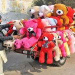 A roadside vendor displays colorful teddy bears loaded on a motorcycle trolley to attract customers
