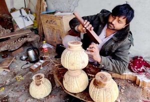 A craftsman meticulously carves wooden pieces into decorative items, showcasing Chiniot’s renowned tradition of fine craftsmanship.