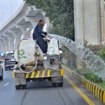 A PHA staffer watering plants at center path of road
