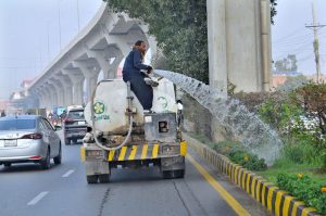 A PHA staffer watering plants at center path of road
