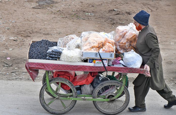 A vendor pushing handcart loaded with edible items to attract the customers