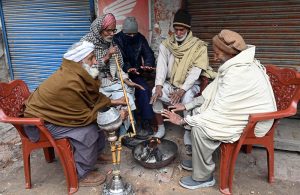 In the severe cold of the provincial capital, elderly people warm their hands by a fire and enjoy a traditional hookah at Chowk Noonarian, Khuda Bakhsh Road