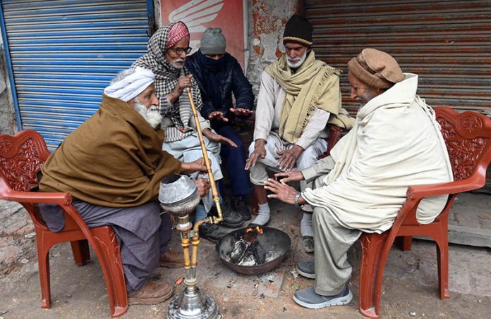 In the severe cold of the provincial capital, elderly people warm their hands by a fire and enjoy a traditional hookah at Chowk Noonarian, Khuda Bakhsh Road