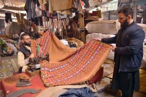A tailor sews a traditional Chitrali woolen shawl for a customer in Chowk Yadgar during the winter season.