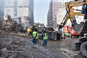 Rescue workers work with heavy machinery to clear the rubble of a burnt building of a multi-story Gul shopping plaza following a massive fire.