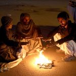 People sit by a roadside fire to keep themselves warm amid the chilly weather in the city