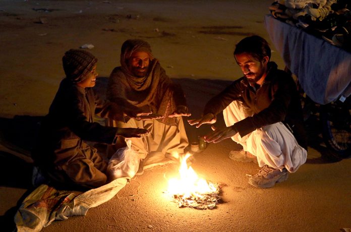 People sit by a roadside fire to keep themselves warm amid the chilly weather in the city