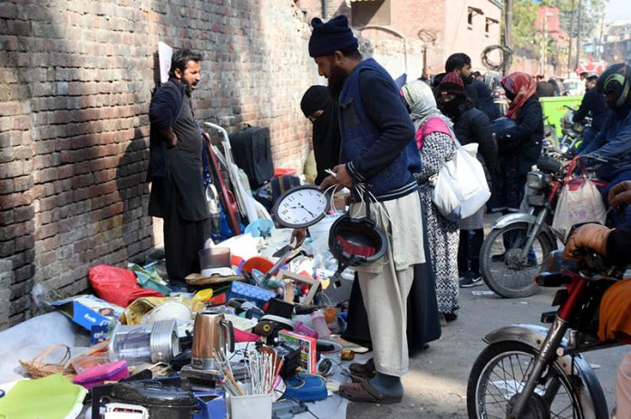 People selecting and purchasing used items from a stall along Mall Road in Provincial Capital