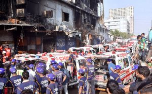 Security personnel stand as rescue workers search the debris for fire victims at Gul Plaza.