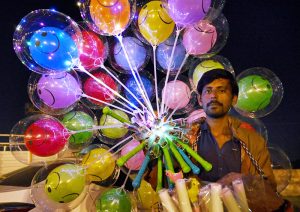 A street vendor sells illuminated balloons at a busy location.