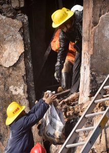 Security personnel stand as rescue workers search the debris for fire victims at Gul Plaza.