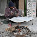 A worker warms himself by burning wood in the bitter cold while crafting a nameplate on a marble slab along Mazang Road