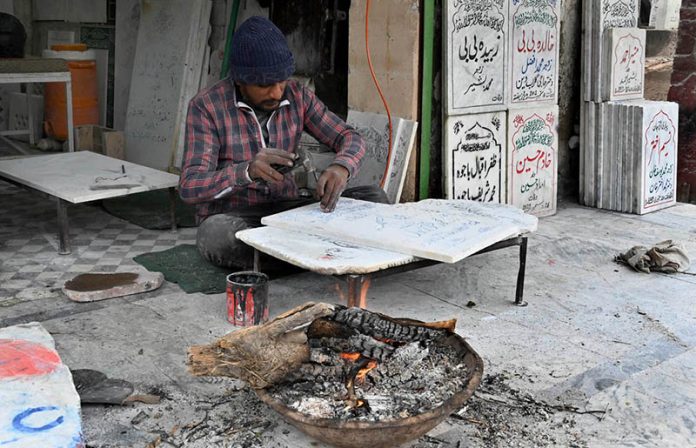 A worker warms himself by burning wood in the bitter cold while crafting a nameplate on a marble slab along Mazang Road