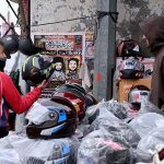 A motorcyclist purchases a helmet from a roadside vendor