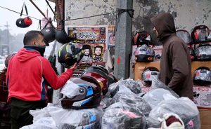 A motorcyclist purchases a helmet from a roadside vendor