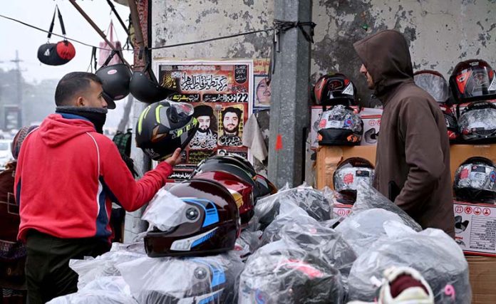 A motorcyclist purchases a helmet from a roadside vendor