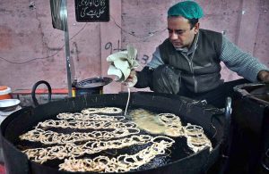 A vendor prepares sweet food item Jalebi to the customers at his roadside setup in the Provincial Capital.