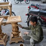 A young worker busy painting wooden tables at his workplace in the city