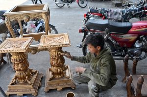 A young worker busy painting wooden tables at his workplace in the city