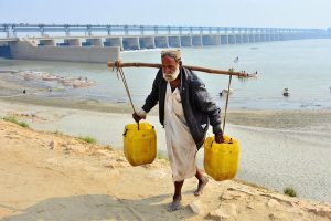 An elderly person carries water cans after filling them at the Indus River.