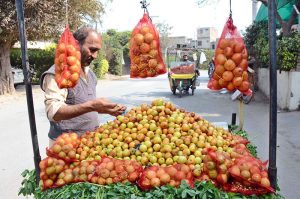 A street vendor arranges freshly harvested seasonal Jujubes on his cart to drawing the attention of passersby along a busy roadside.