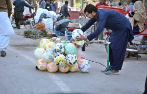 A vendor busy in filling air in footballs to attract customers at his roadside setup.