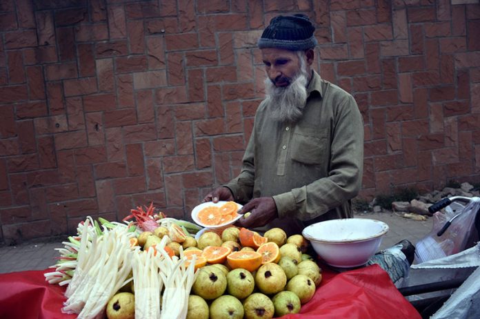 An elderly vendor sells fresh vegetables and fruit salad on his bicycle displayed for sale at a roadside