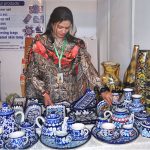 A lady vendor arranges hand-painted famous Multani blue pottery items, including tea sets and decorative vases, at the Blue Fair Exhibition organized by the Women Chamber of Commerce, highlighting intricate floral motifs and centuries-old craftsmanship