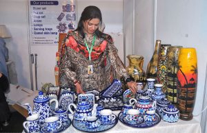 A lady vendor arranges hand-painted famous Multani blue pottery items, including tea sets and decorative vases, at the Blue Fair Exhibition organized by the Women Chamber of Commerce, highlighting intricate floral motifs and centuries-old craftsmanship