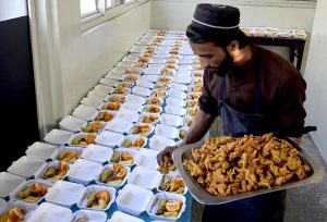 A volunteer arranges iftar meals, placing pakoras in takeaway boxes lined up for distribution during the holy month of Ramazan.
