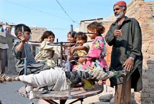 A man swings children on a portable merry-go-round as they enjoy outside their homes.