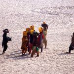 Villager women carry pots filled with water along the banks of the Indus River