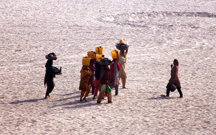 Villager women carry pots filled with water along the banks of the Indus River