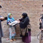 A police officer standing in an alert position while a health worker administers a polio vaccine to a child during a door-to-door vaccination campaign in Dalazak Road Faqirabad area.