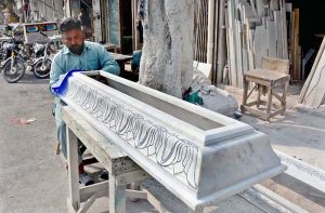 A worker is busy carving decorative patterns on a marble grave model at his work place.
