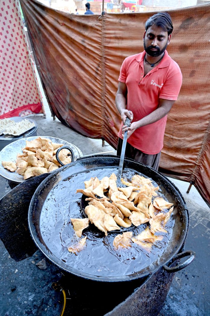 Vendors prepare traditional food items, including Samosas, outside their shop during the holy fasting month of Ramazan