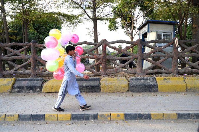 A street vendor on his way displaying colorful balloons to attract customers at the roadside