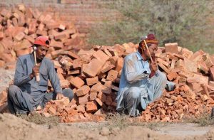Daily wages Labourers break bricks with hammers at a brick kiln for construction sector.