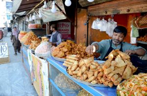 A street vendor serves pakoras and samosas to customers for iftar