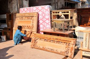 A worker is busy polishing and arranging wooden furniture displayed outside a local workshop to attract customers in the city