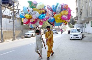 Young street vendors walk through the busy city streets, carrying colorful balloons to attract customers, adding a cheerful touch to the urban bustle.
