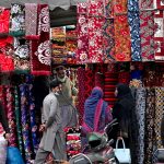 Ladies selecting colorful bedsheets, curtains, and other fabrics from a vendor near Delhi Gate