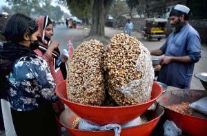 A roadside vendor roasts peanuts and grams and sells various dry fruits to customers in the provincial capital.
