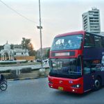 People enjoy a ride on a double-decker bus near the Governor House.