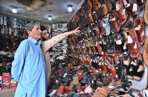 A vendor displays shoes to a customer in his shop at KhanaPul as Eid preparations continue in the Federal Capital.