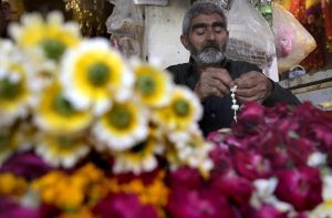 An elderly vendor strings fresh flower garlands at his small roadside setup in Banni Chowk, hoping to attract customers with the vibrant display.