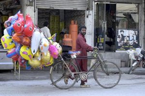 A vendor sells balloons from his bicycle to attract customers along a street.