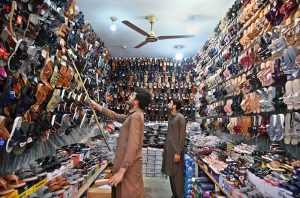A vendor displays shoes to a customer in his shop at KhanaPul as Eid preparations continue in the Federal Capital.