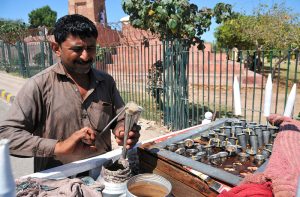 A roadside vendor prepares traditional kulfi using metal molds at his mobile cart to serve customers.